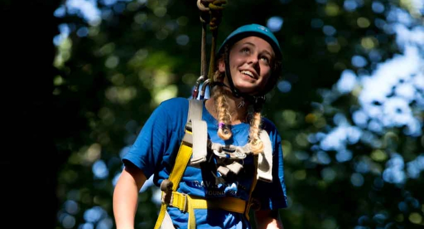 A person wearing safety gear is attached by ropes as they smile. 